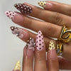 A close-up of a hand displaying various press-on false nails featuring polka dots and ladybug designs in various shades of pi