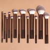 A collection of thirteen professional makeup brushes with dark handles and fluffy, light gray bristles arranged horizontally.