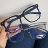 Una mano sostiene unas gafas cuadradas vintage con marcos oscuros y lentes tintados azules.