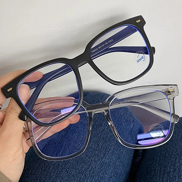 Una mano sostiene unas gafas cuadradas vintage con marcos oscuros y lentes tintados azules.