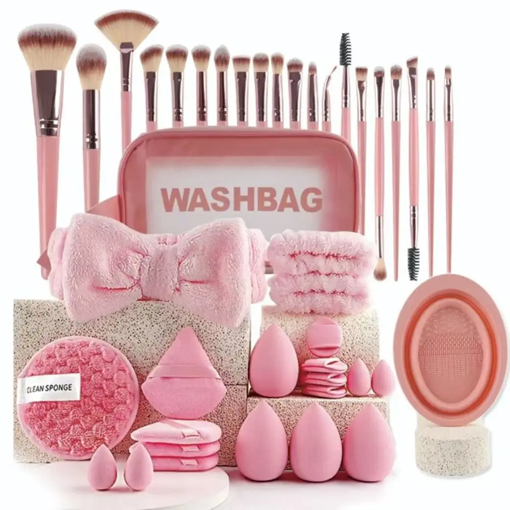 A pink washbag and various makeup brushes, sponges, and tools are displayed on a surface.