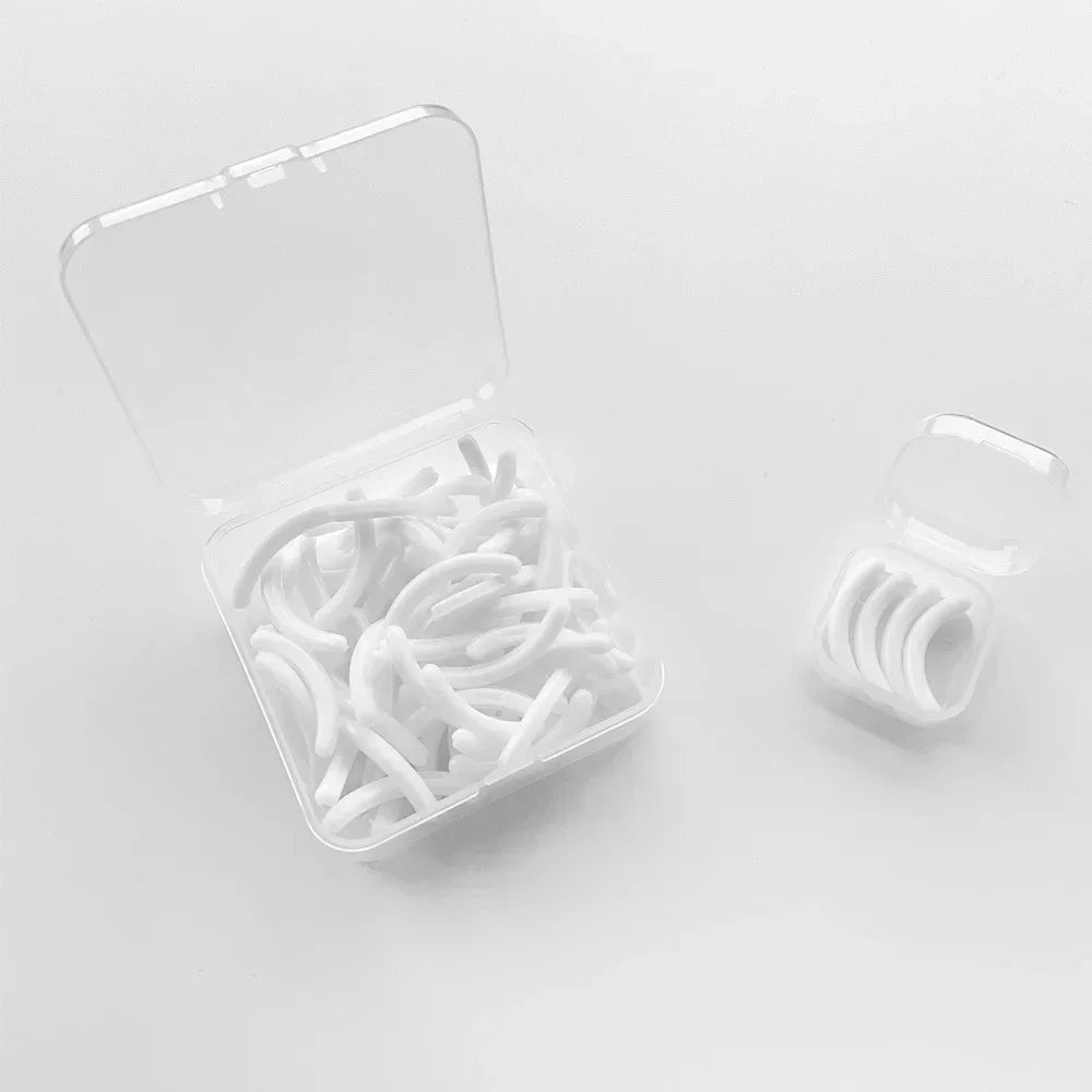 A clear plastic container filled with 30 white reusable silicone eyelash curler pads.