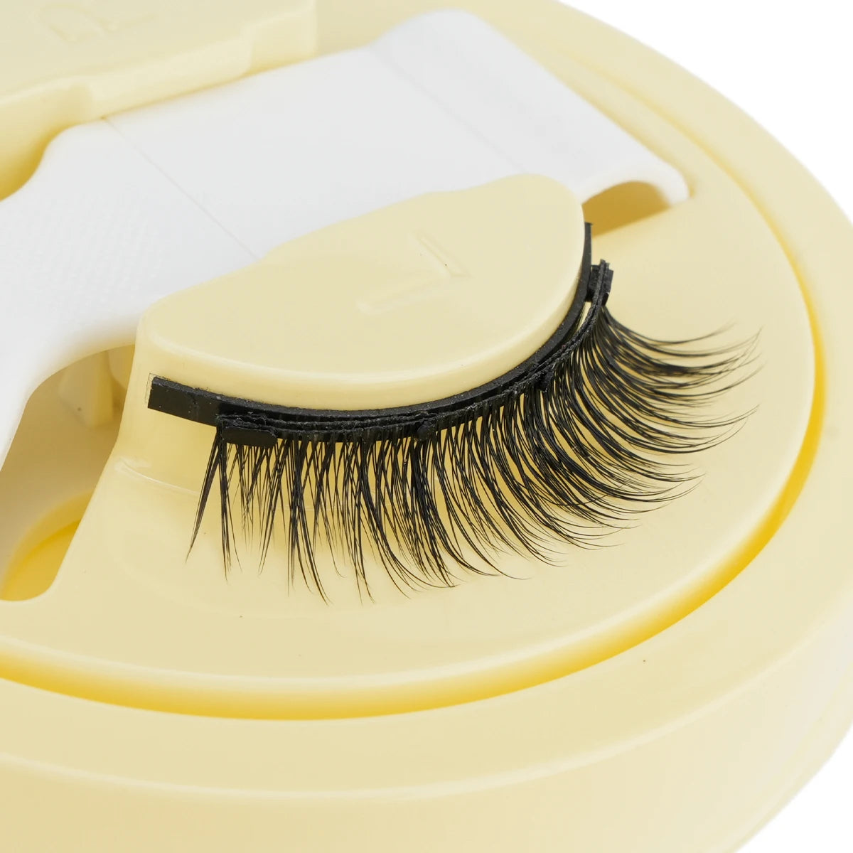 Un ensemble de faux cils magnétiques réutilisables noirs attachés à un support en plastique jaune clair.