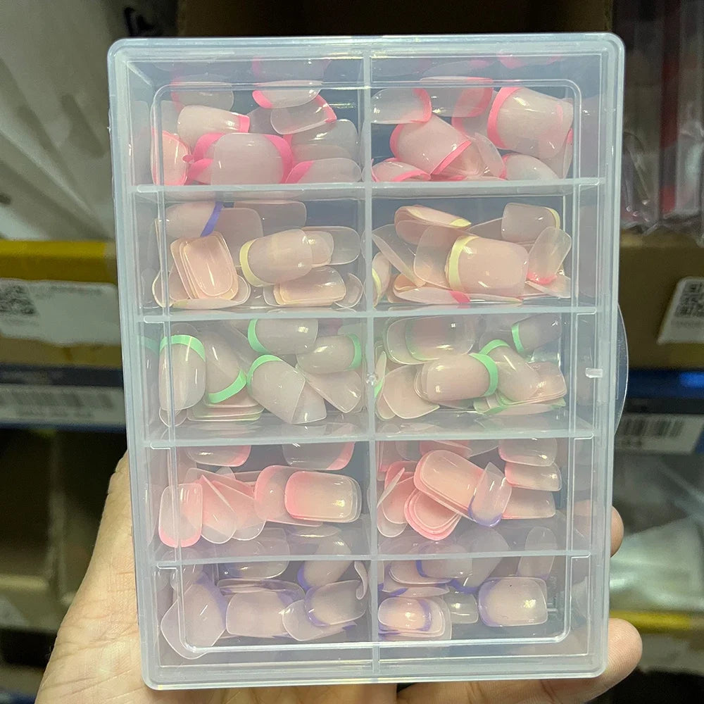 Une boîte en plastique transparent contenant divers tons de rose et de violet de faux ongles acryliques.