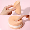 A hand is squeezing a peach-colored makeup sponge puff, showing its texture and shape.