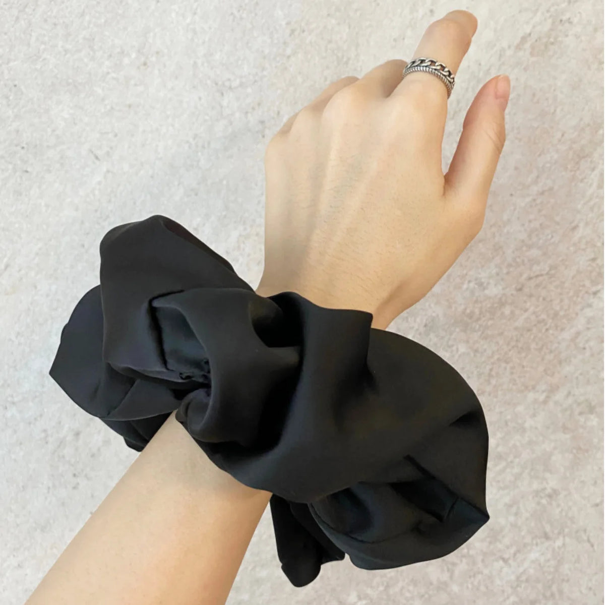 Une main portant un élastique pour cheveux en mousseline de satin noir, montrant un style élégant.