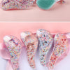 Un ensemble de peignes à cheveux en plastique colorés et scintillants pour enfants et adultes, présentés sur un tissu rose.