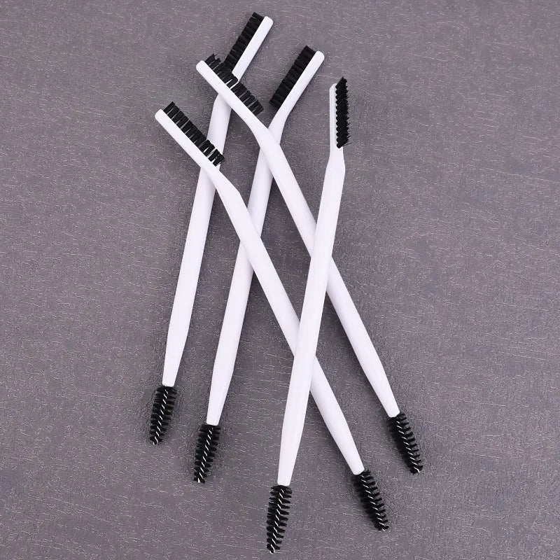 A set of white dual-ended eyelash curlers and brow brushes arranged diagonally on a gray surface.