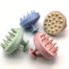 Three silicone body and scalp massage brushes in light blue, beige, and pink are displayed on a white surface.