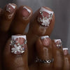 A close-up of a hand displaying press-on fake nails with white tips and floral silver embellishments.