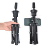 A black adjustable wig stand tripod is shown being held by a hand, with the stand positioned next to a smartphone.