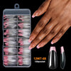 Une main tient un contenant en plastique transparent de 120 pointes de ongles en acrylique courbe C extra longues.