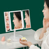 A woman is using a foldable LED makeup mirror with magnification on a white table.