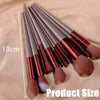 A set of 13 professional makeup brushes with brown and copper handles laid out on a beige surface.