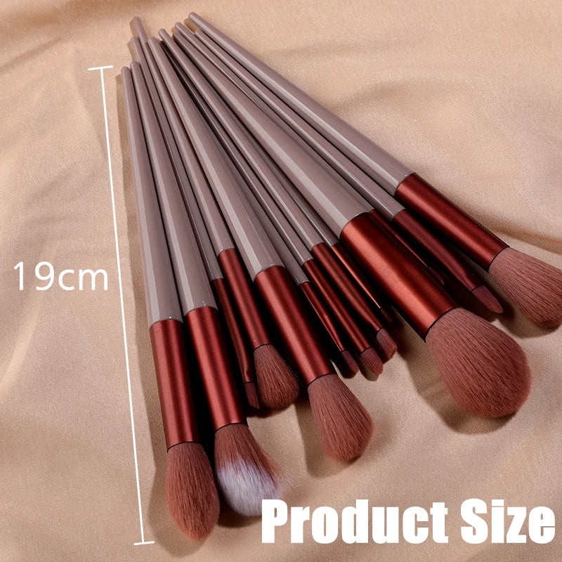 A set of 13 professional makeup brushes with brown and copper handles laid out on a beige surface.