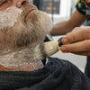 A person is using a brush to apply shaving cream or lather to their beard.