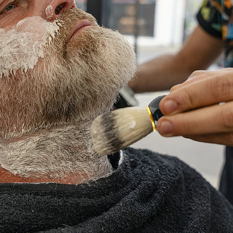 A person is using a brush to apply shaving cream or lather to their beard.