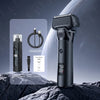 A black portable electric shaver is shown next to its charging cable and manual on a rocky surface.