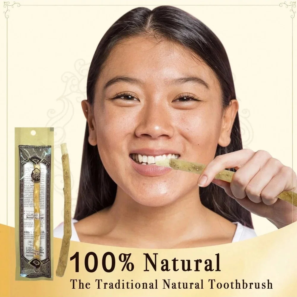 A young woman holds a traditional wooden miswak toothbrush to her mouth against a light background.