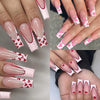 Close-up of long acrylic nails painted with a nude pink matte French manicure featuring small red hearts.