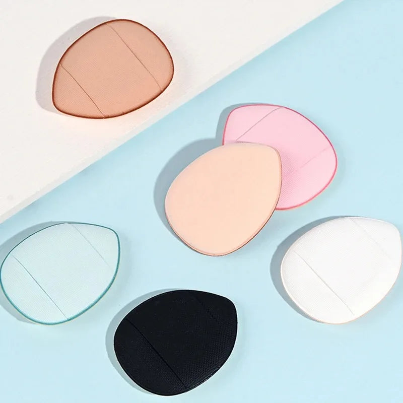 Une collection de mini éponges de fond de teint dans des tons de rose, beige et blanc sont présentées sur un fond bleu clair.