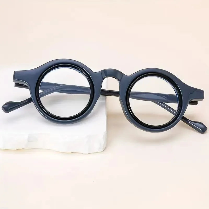 Une paire de lunettes de lecture transparentes et ajustables bleu foncé posées sur une surface blanche.