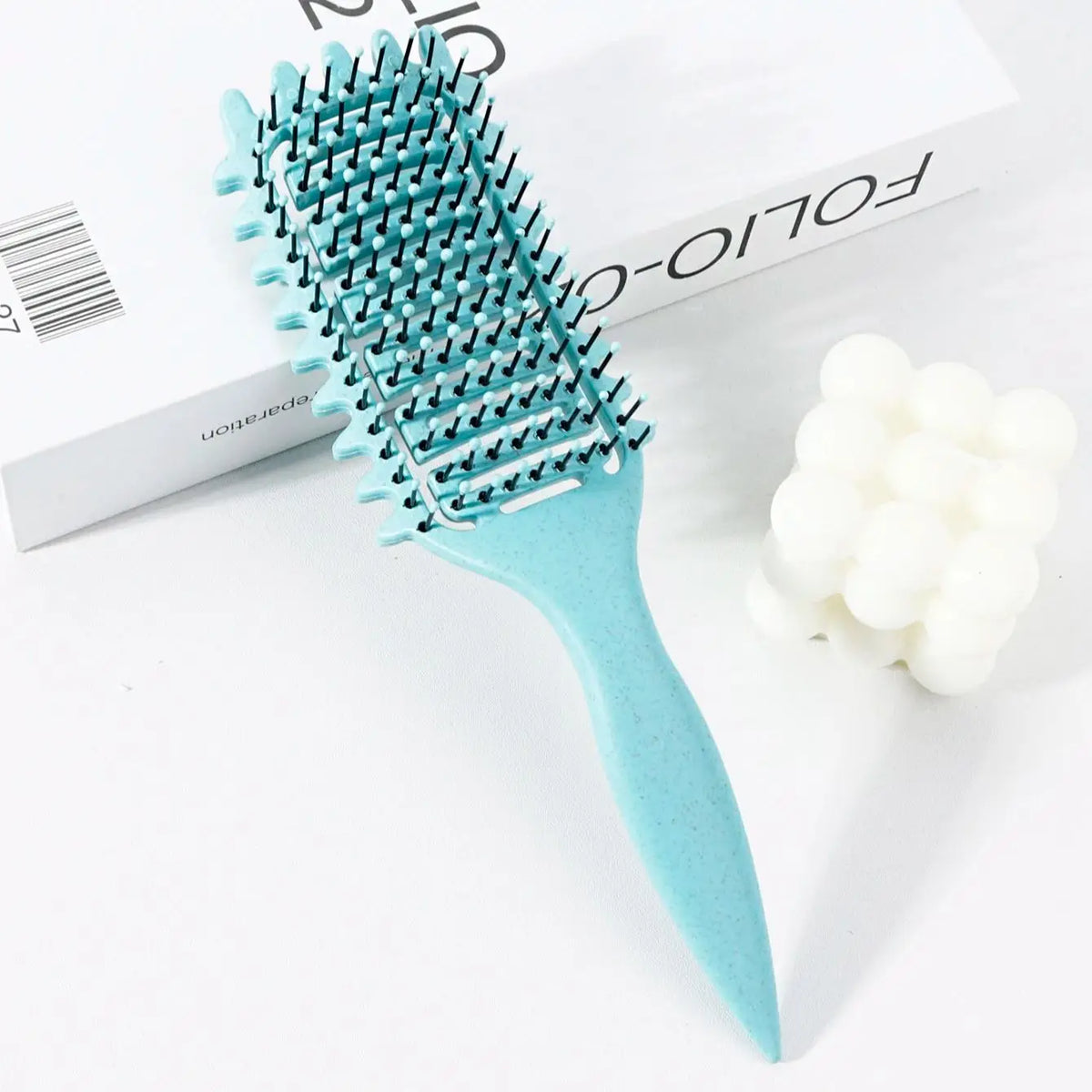 Peigne pour cheveux bouclés bleu clair professionnel avec poils bleu sarcelle, à côté d'un accessoire en caoutchouc blanc.