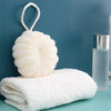 A white exfoliating bath bubble ball with a soft mesh sponge resting on a white towel against a blue background.