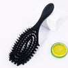 Black bristle hollow arc styling comb resting on a white surface next to a slice of lime.