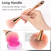 A hand holds a rose gold long handle dusting brush used for makeup application or removal.