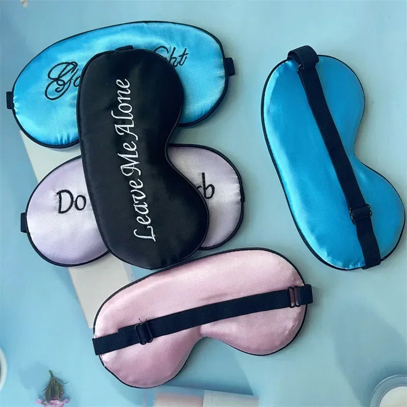 A collection of silk sleep masks in various shades of blue and pink with embroidered text