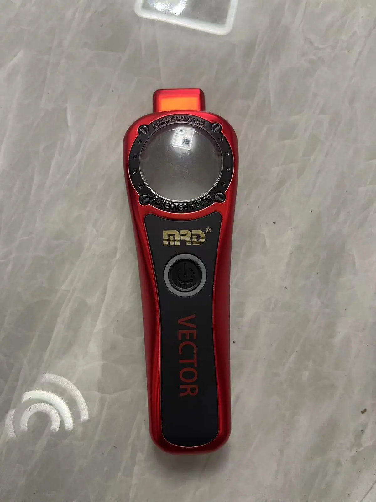 A red professional electric hair trimmer with a silver housing and black grip is shown on a light surface.