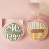 A pair of soft makeup sponge puffs in green and yellow are displayed on a pink background.