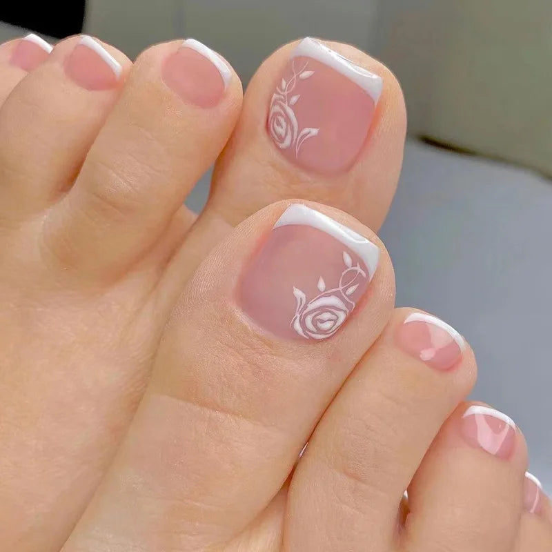 Nahaufnahme einer Hand, die wiederverwendbare falsche Zehennägel im französischen Design mit zarten rosa und weißen Blumenakz