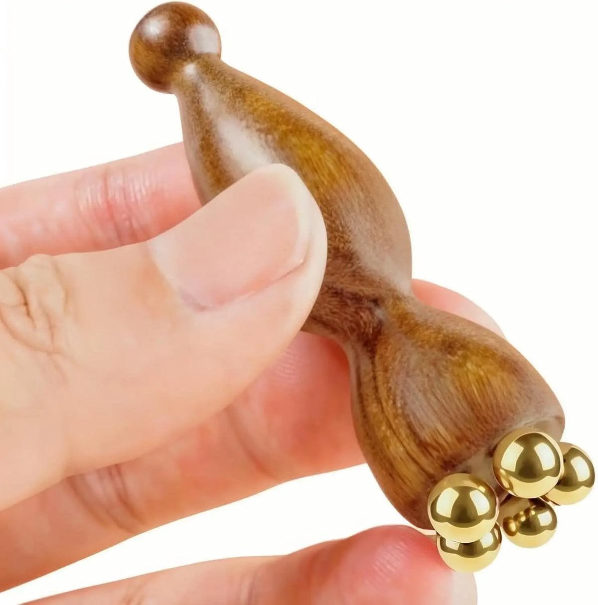 A hand holds a natural wood facial and scalp massage comb with golden ball tips.