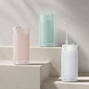 A collection of three portable cordless oral irrigators in mint green, pink, and white are displayed on a light-colored shelf