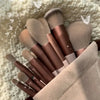 A collection of 22 professional makeup brushes in various shades of brown and beige resting on a fluffy white surface.