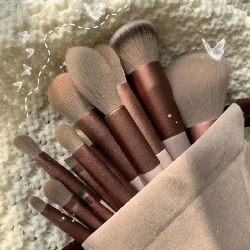 A collection of 22 professional makeup brushes in various shades of brown and beige resting on a fluffy white surface.