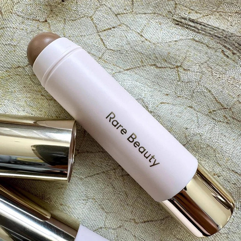 A tube of Rare Beauty liquid bronzer contour foundation stick with a nude-toned product visible on the tip.