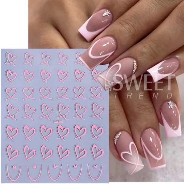 A hand displays a manicure featuring pink and white heart nail decals on fingernails.