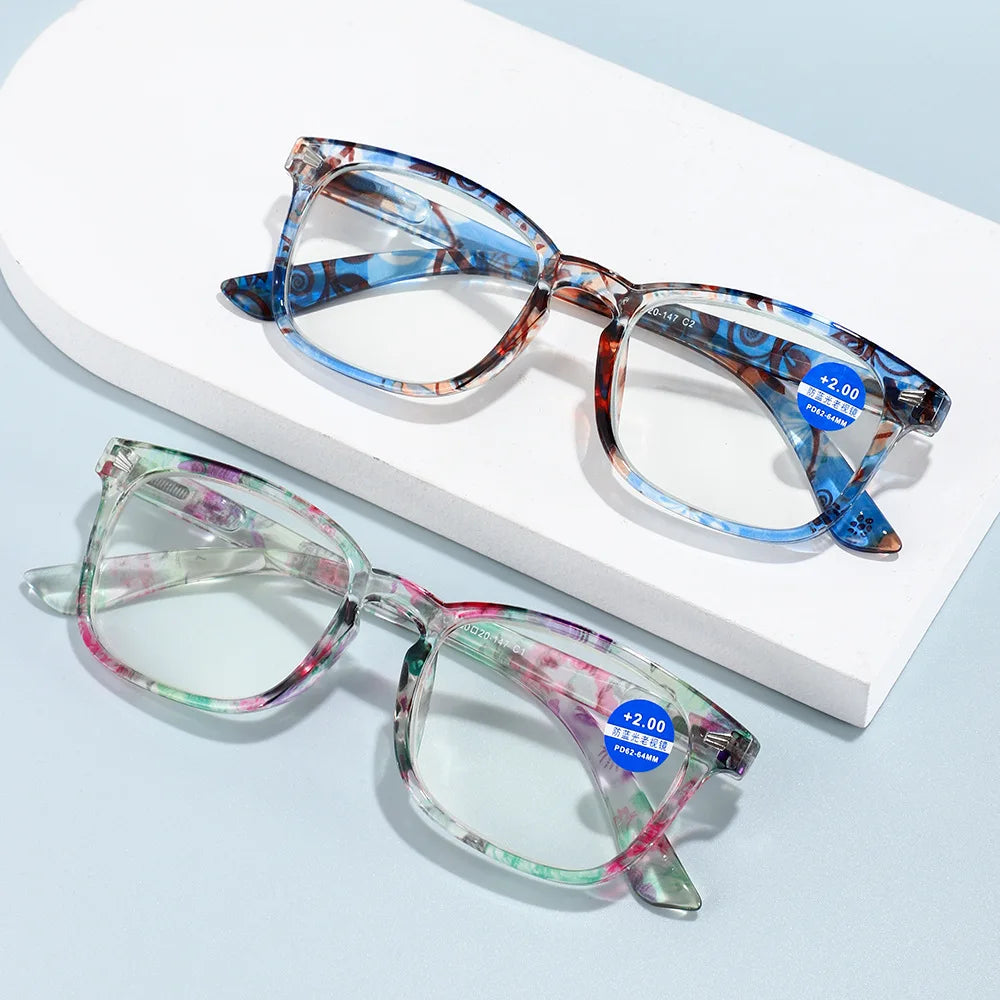 Pair of blue and pink gradient high definition magnifying reading glasses resting on a white box.