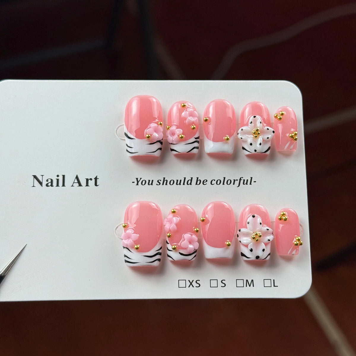 A display of hand-painted pink resin nail art carvings with gold accents in various sizes.