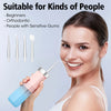 A woman is using a pink portable oral irrigator device on her teeth.