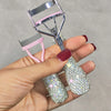 A hand holds a professional eyelash curler set with pink and silver components.