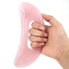 Une main tient une planche de massage guasha en pierre naturelle rose et lisse.