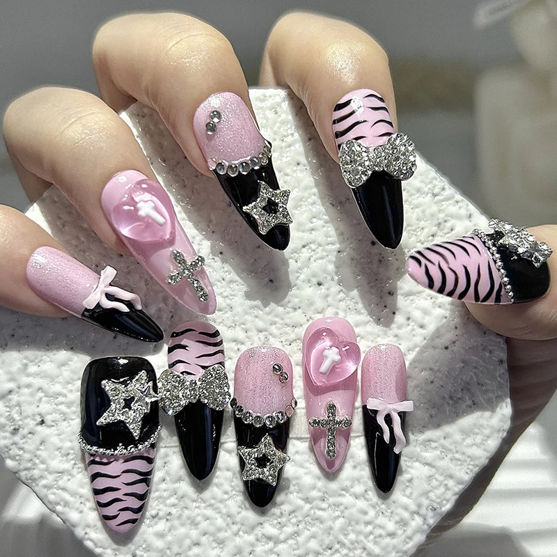 A hand displays a set of press-on nails featuring black, pink, and zebra print designs with glitter diamonds and accents.