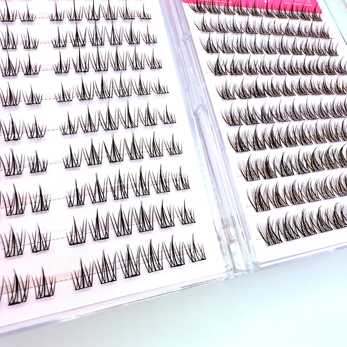 A close-up view of adhesive-free individual lash clusters in various lengths and styles arranged on a clear plastic tray.