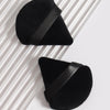 A black triangular cosmetic powder puff set with a black strap resting on a white striped surface.