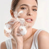 Una mujer está aplicando un exfoliante corporal de luffa natural y una esponja de baño en su rostro con espuma blanca.