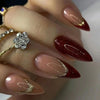 Close-up of a hand displaying long, coffin-shaped press-on false nails with a deep burgundy color and gold glitter accents.